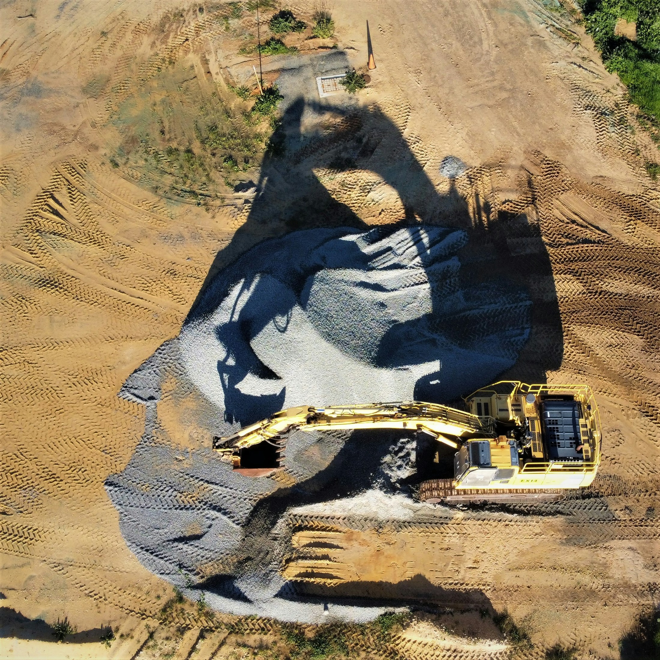 A yellow excavator on a bed of grey aggregate, viewed from above