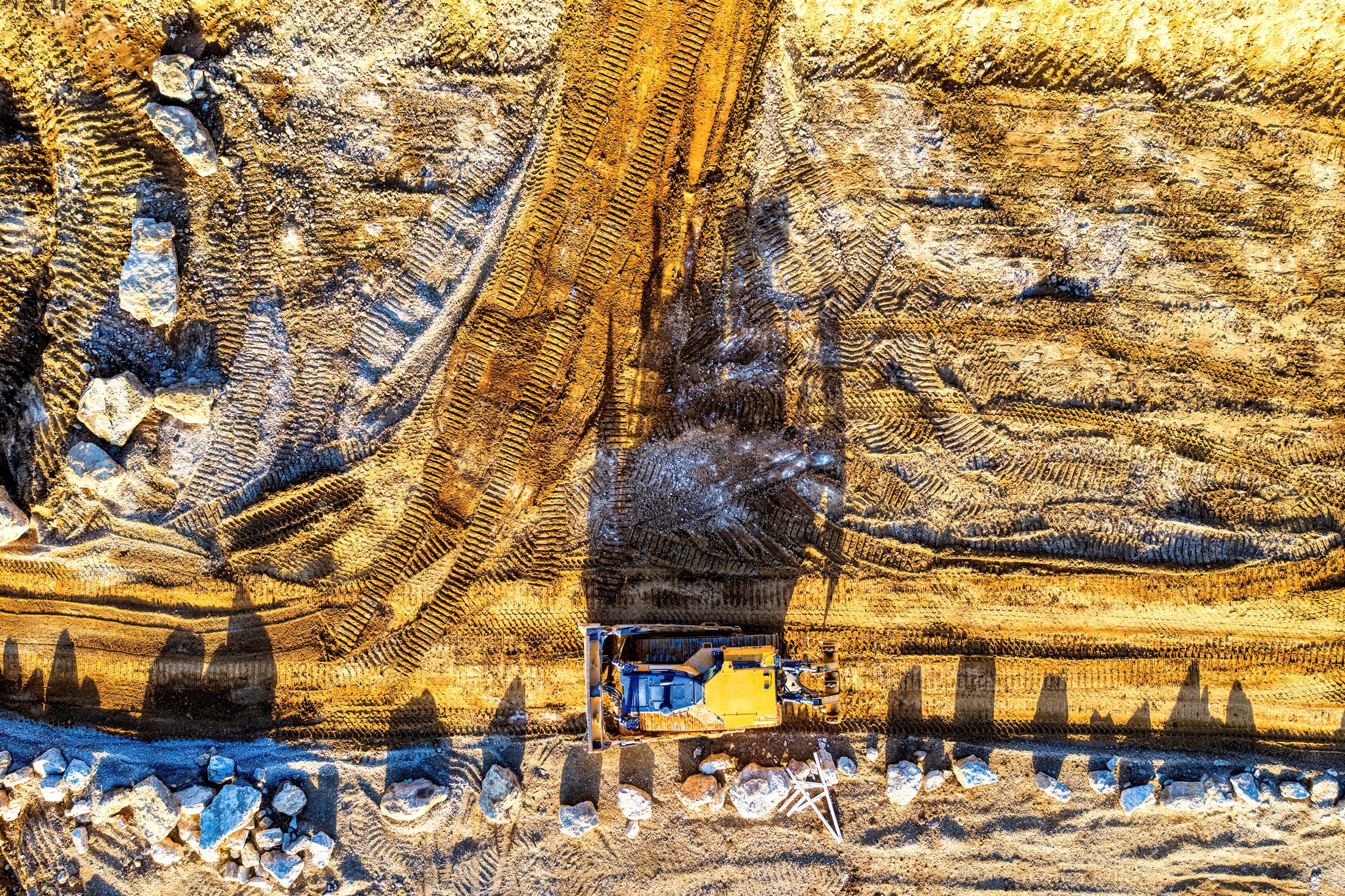 Aerial view of a yellow earthmoving machine and vehicle tracks on a large site