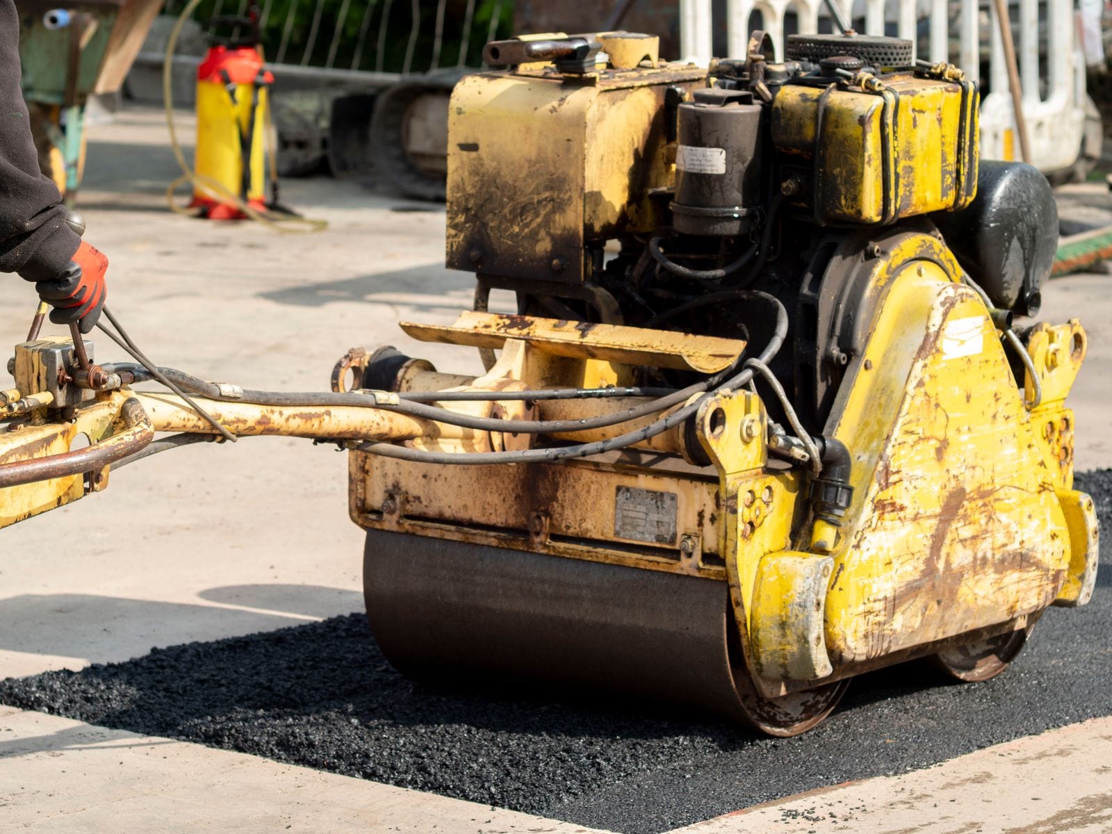 A walk-behind roller compacting a patch of fresh asphalt