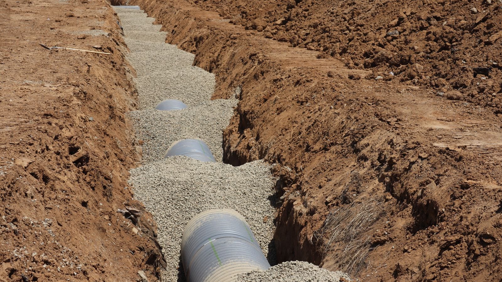 A corrugated drainage pipe partly surrounded by aggregate in an excavated trench
