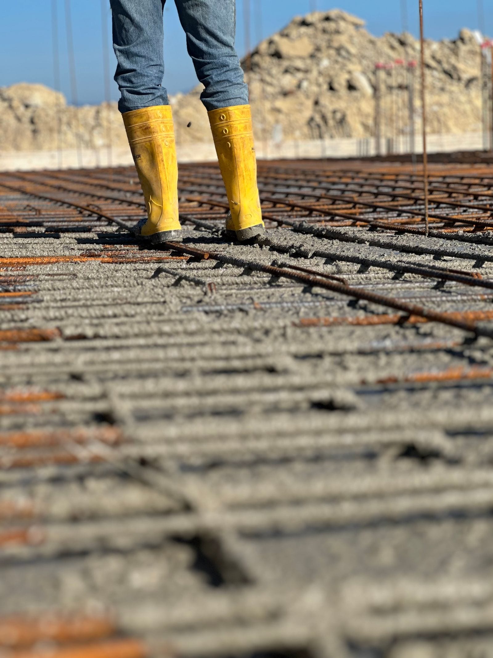 Yellow work boots above steel reinforcement and freshly placed concrete